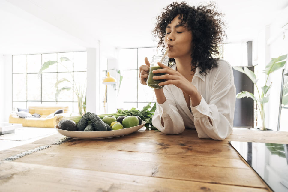 Woman drinking green juice with green foods next to her. (Getty Images)