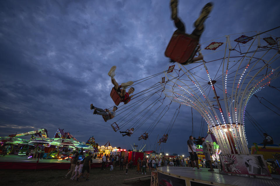 People enjoy a swing ride at a fair in Hagioaica, Romania, Thursday, Sept. 14, 2023. For many families in poorer areas of the country, Romania's autumn fairs, like the Titu Fair, are one of the very few still affordable entertainment events of the year. (AP Photo/Andreea Alexandru)