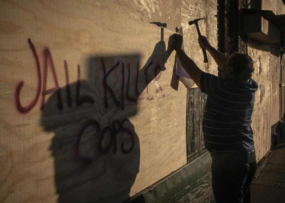 Un individuo clava tablones en el frente del Mercado Central, un mercado mayormente hispano de la calle Lake Street de Minneapolis, que ha sido muy golpeada por la destrucción causada por las protestas por la muerte de George Floyd. Foto del 30 de mayo del 2020. (AP Photo/Bebeto Matthews)