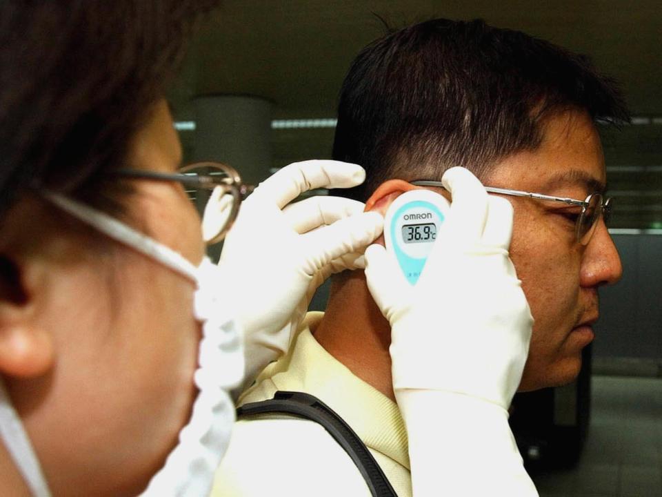 A  doctor takes the temperature of a passenger before he boards a plane at Baiyun International Airport in Guangzhou, capital of south China's Guangdong province in 2003.
