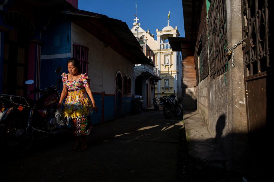 Una mujer camina hacia sus labores por un callejón a la luz de la mañana, con el fondo de una iglesia católica en La Ceiba, Guatemala. Con el paso del tiempo, muchos hombres han migrado para buscar nuevas oportunidades de enviar dinero a sus familias, cambiando el rostro del pueblo con las remesas.