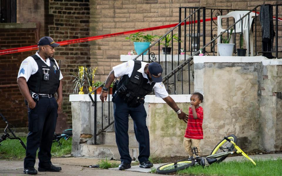 A Chicago police officer helps a child walk through an area being investigated after two men were shot  - AP