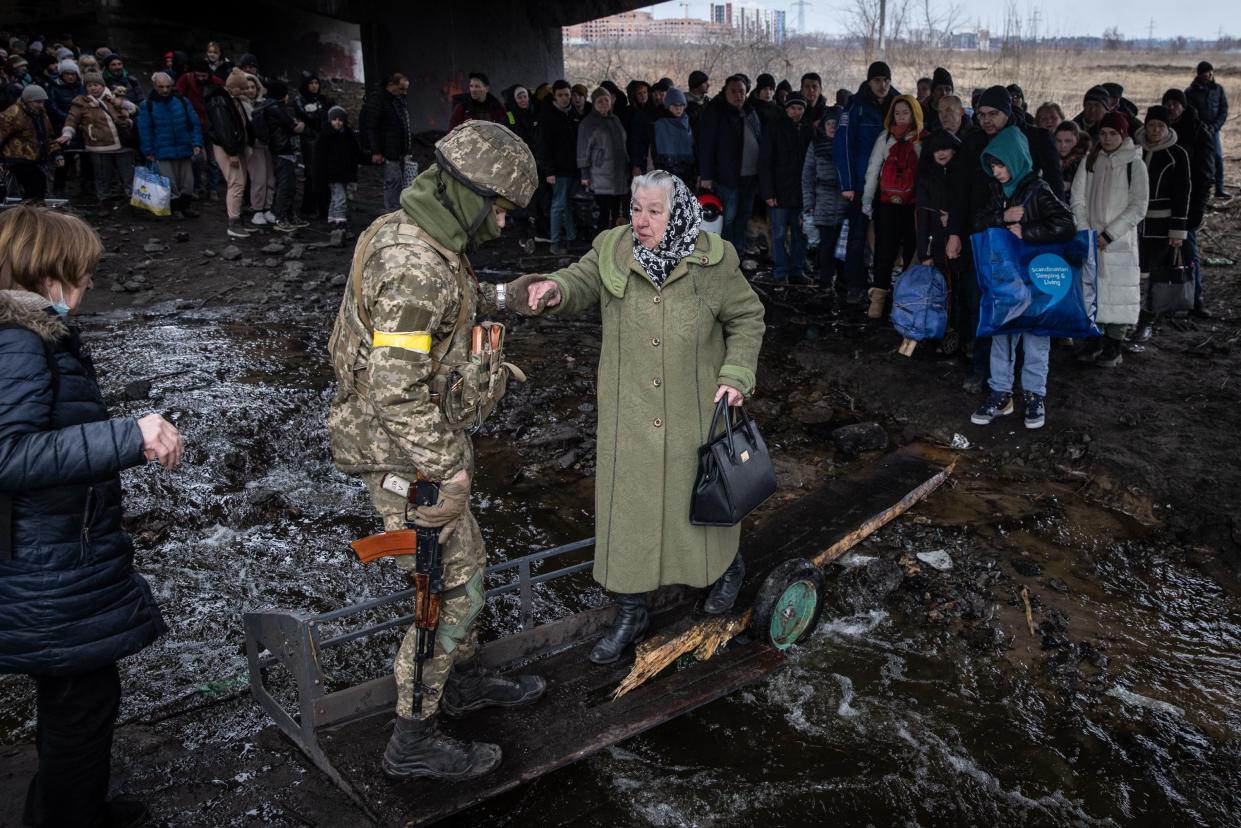 A woman is assisted by a member of the Ukrainian military as she flees heavy fighting in Irpin via a destroyed bridge as Russian forces entered the city on March 07, 2022, in Irpin, Ukraine.