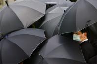 FILE PHOTO: A mourner wearing a mask to protect himself from SARS stands under an umbrella during the funeral of SARS doctor Tse Yuen-man in Hong Kong