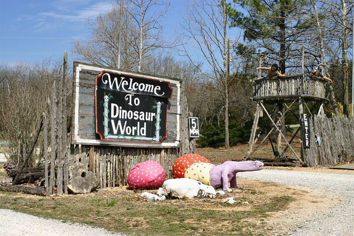 Abandoned Dinosaur World, Beaver, Arkansas, welcome sign with painted dinosaur eggs and a baby dinosaur being born, rustic wooden fence, bare trees in winter, a sunny blue sky