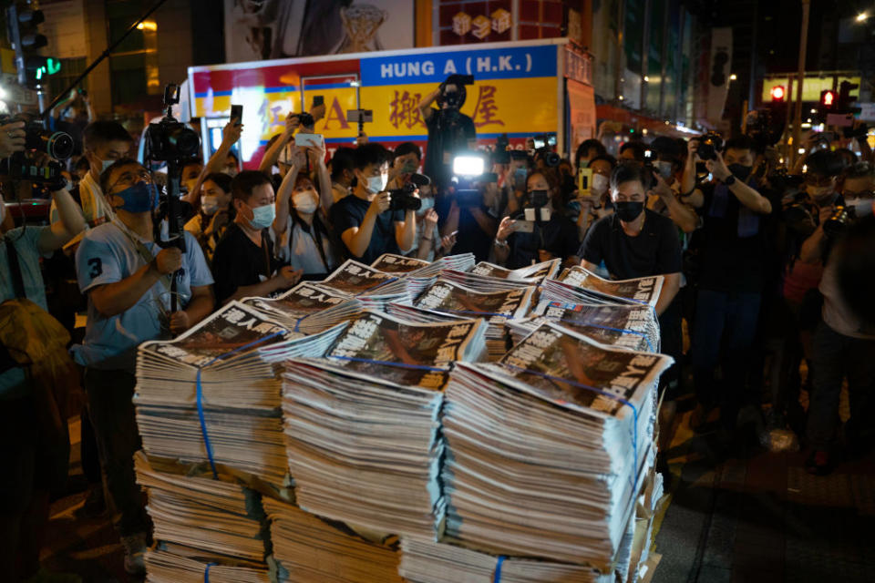 Stacks of the final edition of the Apple Daily surrounded by people.