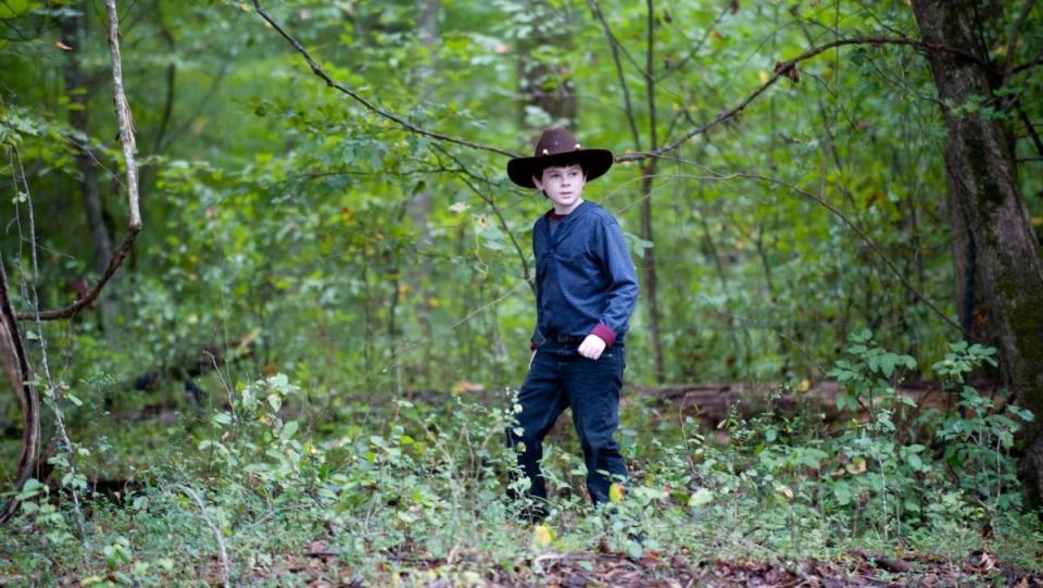 Chandler Riggs as Carl Grimes wearing Rick's Hat and walking through the forest