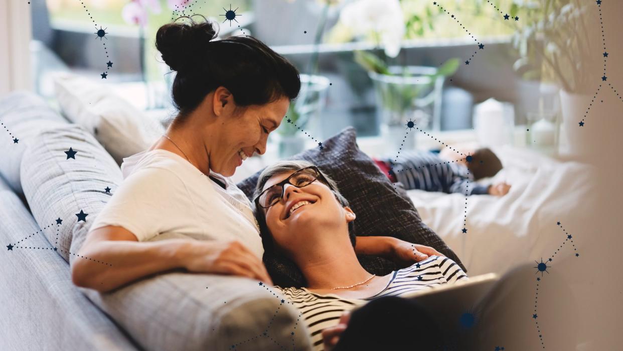 A couple smiles at each other while laying on a couch