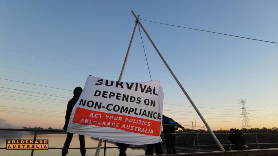 He is seen with a banner which reads: “Survival depends on non-compliance. Act your politics.” Picture: Blockade Australia