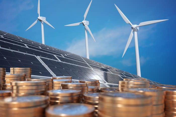 Stacks of coins with wind turbines and solar panels in the background