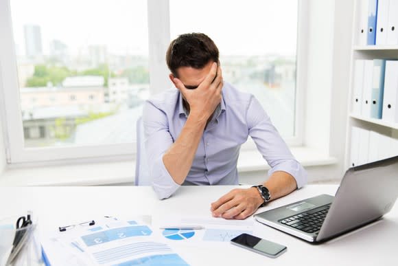 A man looking at his laptop with his head in his hand.