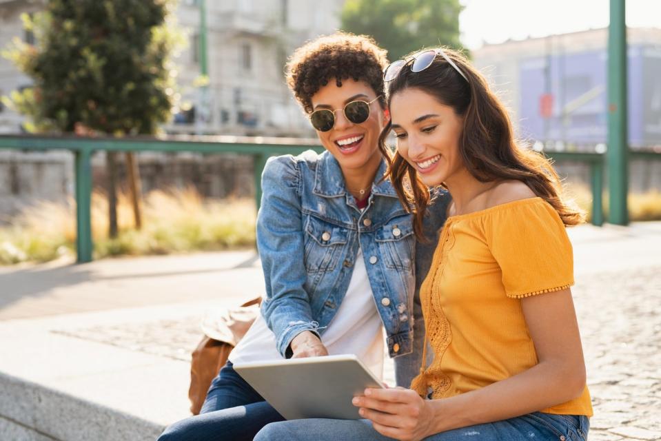 Two people smile while looking at a tablet outdoors.