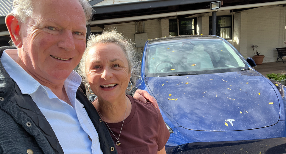 Steve Brine and Tracey McClintock, in their 60s in front of their blue Tesla Model Y on an outback journey in Australia. 