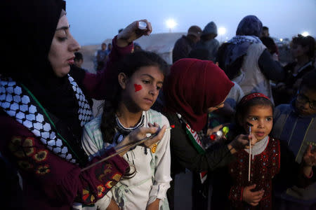 Palestinian artist Reham al-Emawi paints on the face of a girl during a protest at the Israel-Gaza border in the southern Gaza Strip April 12, 2018.REUTERS/Samar Abo Elouf