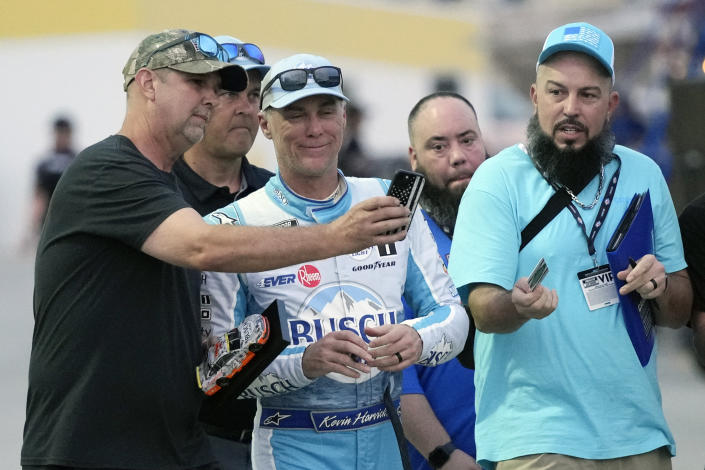 Fans takes selfie photos with Kevin Harvick, center, in the garage area during a practice session for the NASCAR Daytona 500 auto race at Daytona International Speedway, Friday, Feb. 17, 2023, in Daytona Beach, Fla. (AP Photo/John Raoux)