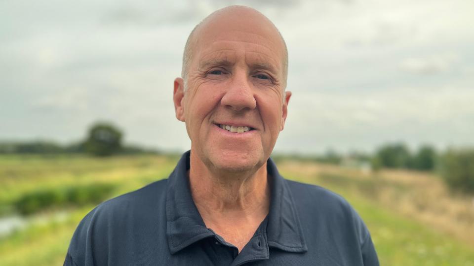 Richard Astle stood in a field wearing a navy blue polo shirt