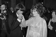 ARCHIVO – En esta fotografía del 16 de diciembre de 1977 el diseñador Kenzo Takada besa la mano de la actriz italiana Gina Lollobrigida después de que ella le entregara un premio a uno de los 10 hombres más elegantes del mundo en Roma, Italia. La familia del diseñador informó el domingo 4 de octubre de 2020 que Takada falleció por complicaciones de COVID-19 en un hospital de Neuilly-sur-Seine, cerca de París. Tenía 81 años. (AP Foto, archivo)