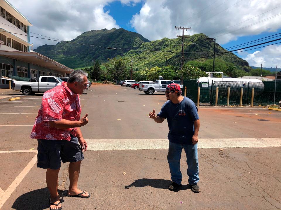 Glen Kila, left, and Brad Suzuki, right, flash the Hawaii "shaka" signs with their hands and give slight bows, demonstrating how they greet people using social distancing to curb the spread of coronavirus in Waianae, Hawaii.