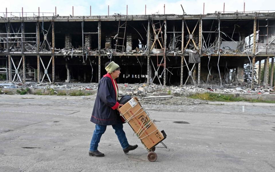 A local resident carries her cart by a destroyed building in Izyum, Kharkiv region, on September 28 - SERGEY BOBOK/AFP