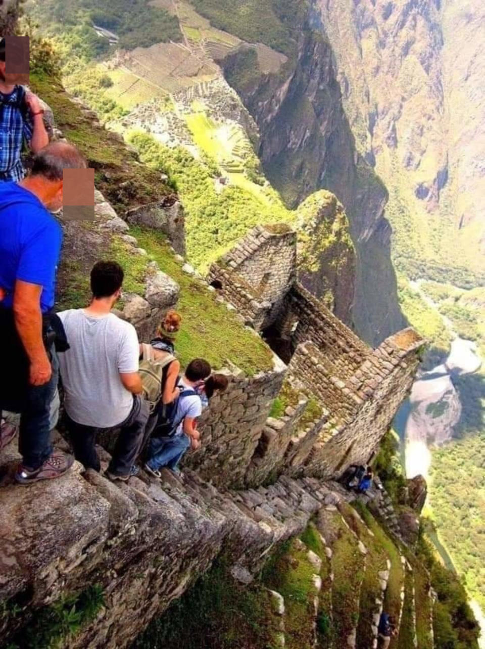 Overhead view of people walking down extremely steep, narrow cobblestone stairs alongside a cobblestone edifice