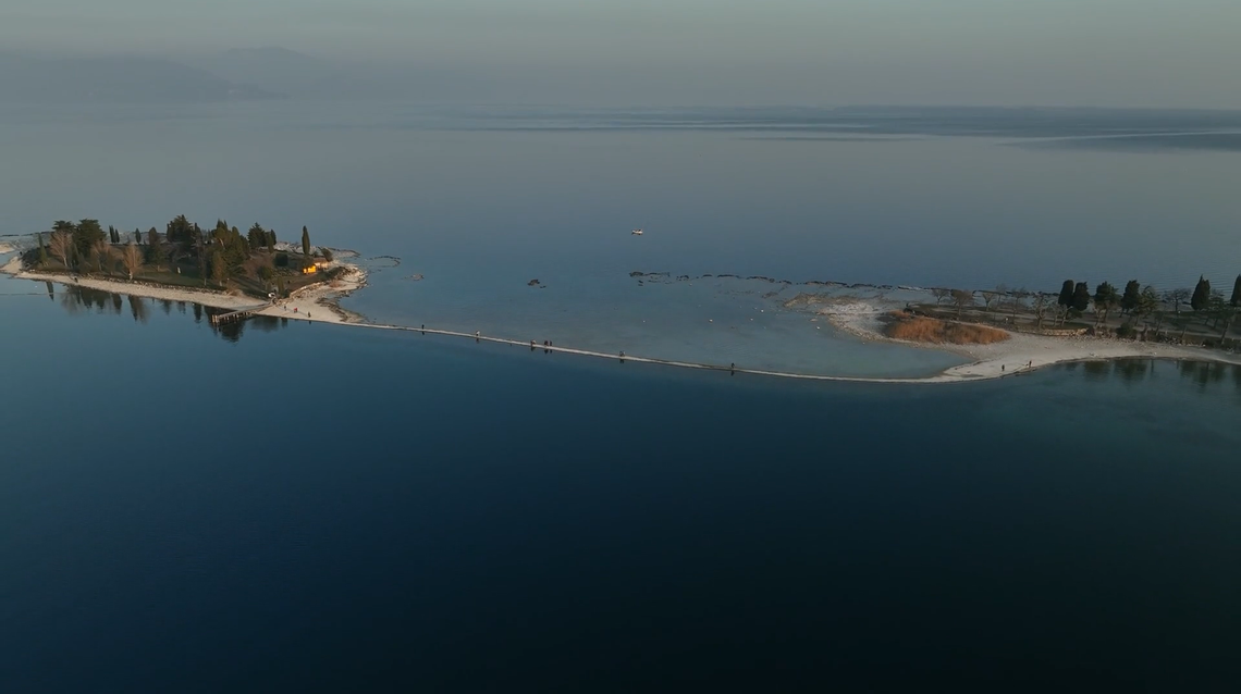 Drone footage shows the island (left) and the mainland (right) with a narrow pathway in between.