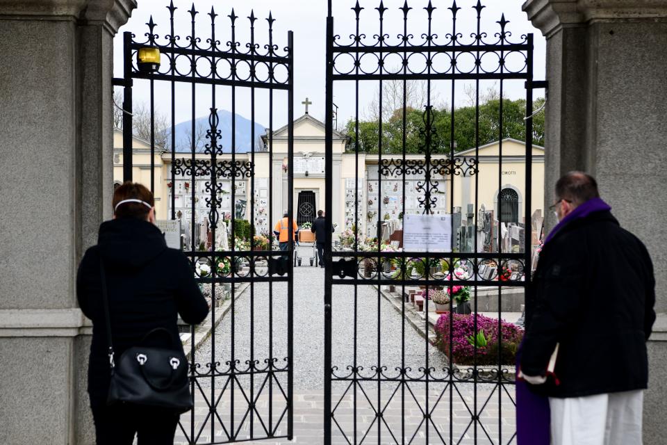 Un familiar de una persona fallecida y un sacerdote esperan en el exterior de un cementerio, que permanece cerrado, la llegada de un féretro para celebrar el funeral, en la localidad italiana de Bolgare, en Lombardía, Italia (PIERO CRUCIATTI/AFP via Getty Images)