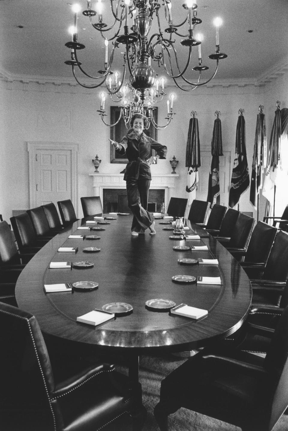 Betty Ford stands on the Cabinet Room table at the White House wearing pants.