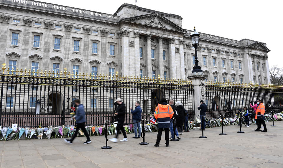 People leave flowers and take photos outside the gates of Buckingham Palace in London, a day after the death of Britain's Prince Philip, Saturday, April 10, 2021. Britain's Prince Philip, the irascible and tough-minded husband of Queen Elizabeth II who spent more than seven decades supporting his wife in a role that mostly defined his life, died on Friday. (AP Photo/Alberto Pezzali)
