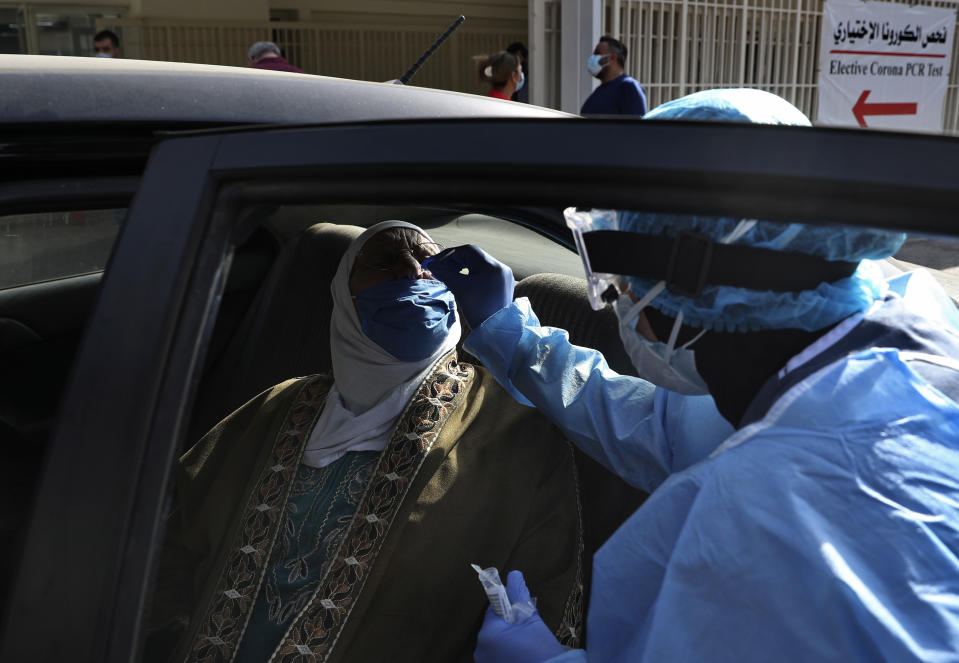 A nurse in protective clothing takes a swab from a woman in her car near the emergency entrance of a coronavirus testing center in the Rafik Hariri University Hospital in Beirut, Lebanon, Monday, Jan. 11, 2021. Lebanon's caretaker prime minister said Monday the country has entered a "very critical zone" in the battle against coronavirus as his government mulls tightening nationwide lockdown announced last week. (AP Photo/Bilal Hussein)
