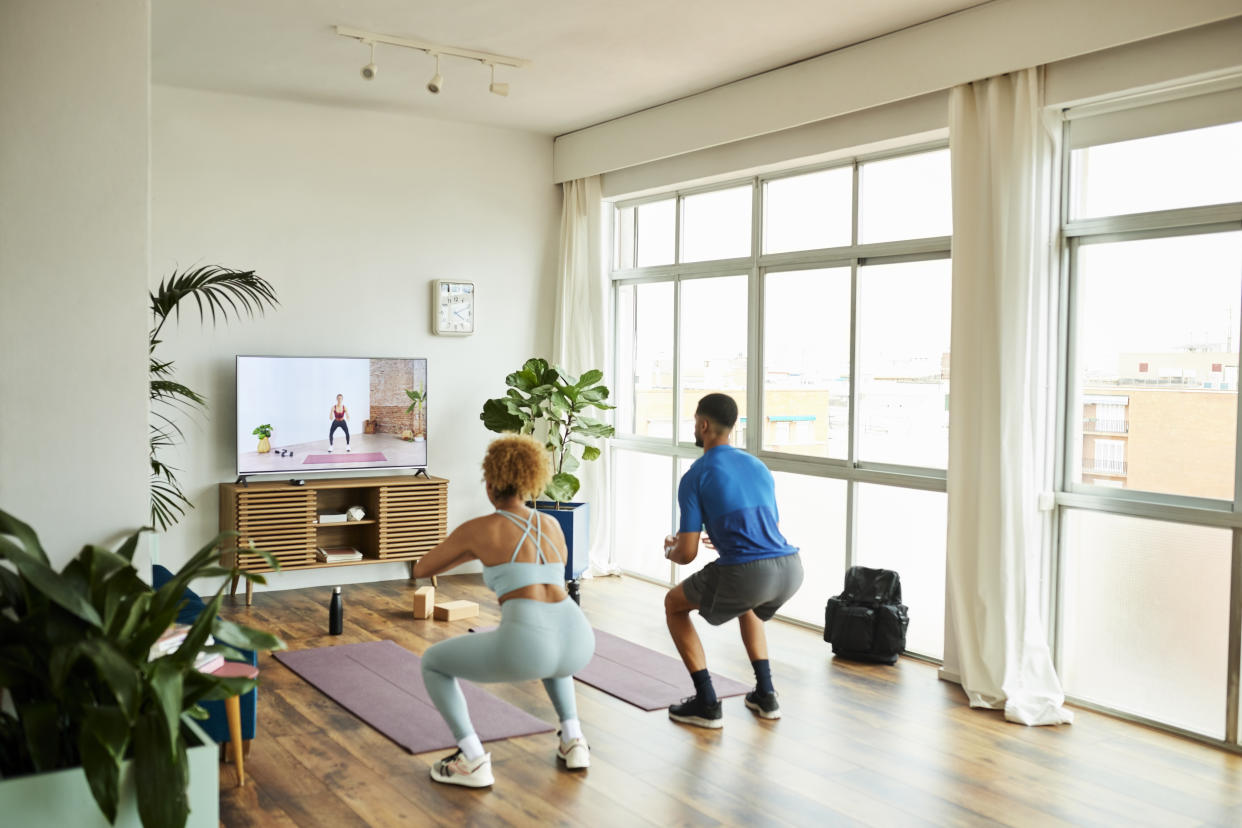 Man and woman doing squats at home. (Getty Images)