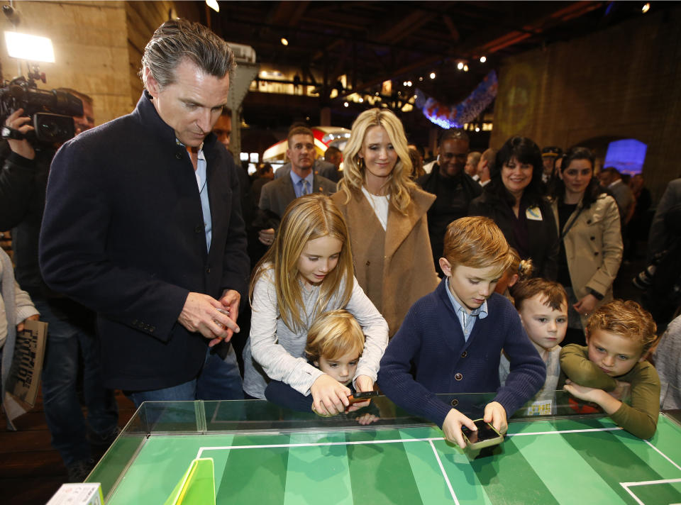 FILE -- In this Jan. 6, 2019 file photo Governor-elect, Lt. Gov. Gavin Newsom, left, and his wife, Jennifer Siebel Newsom, center, watch their children, daughter Montana, second from left, and sons, Dutch, foreground and Hunter, foreground fourth from left, operate robot games during an Inaugural Family Event at the California Railroad Museum, Sacramento, Calif. Since the inaugural, Siebel Newsom often attends events with her husband but also works on issues of her own including equal rights for women. (AP Photo/Rich Pedroncelli, File)