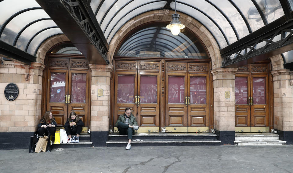 People sit on the front steps of the currently closed Palace Theater which when it reopens will continue its run of the play 'Harry Potter and the Cursed Child' In London, Tuesday, April 20, 2021. (AP Photo/Alastair Grant)