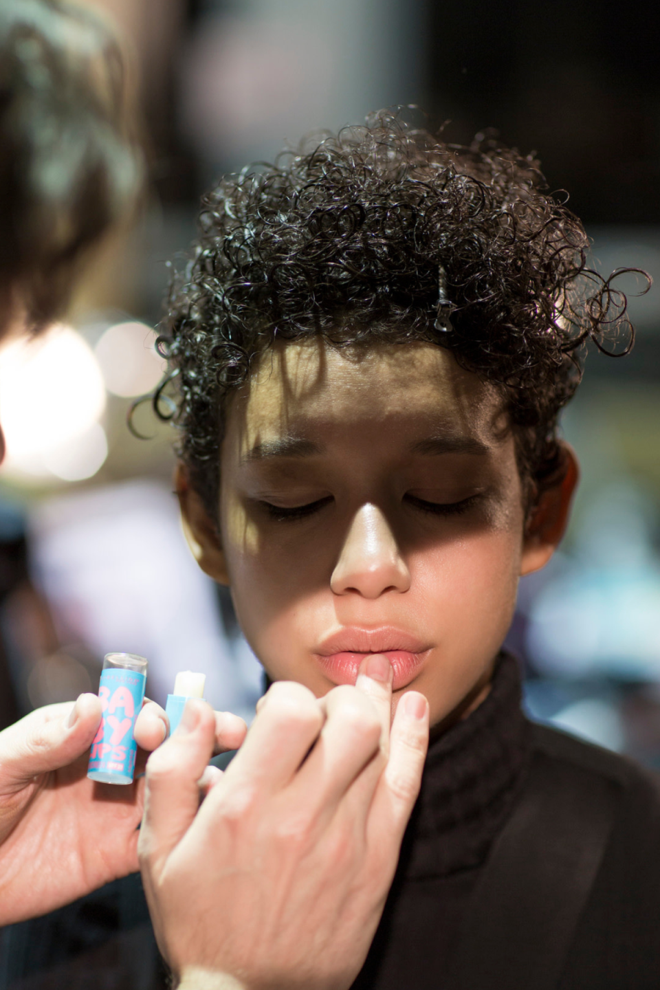 A makeup artist applies makeup on a curly broccoli haircut on a model