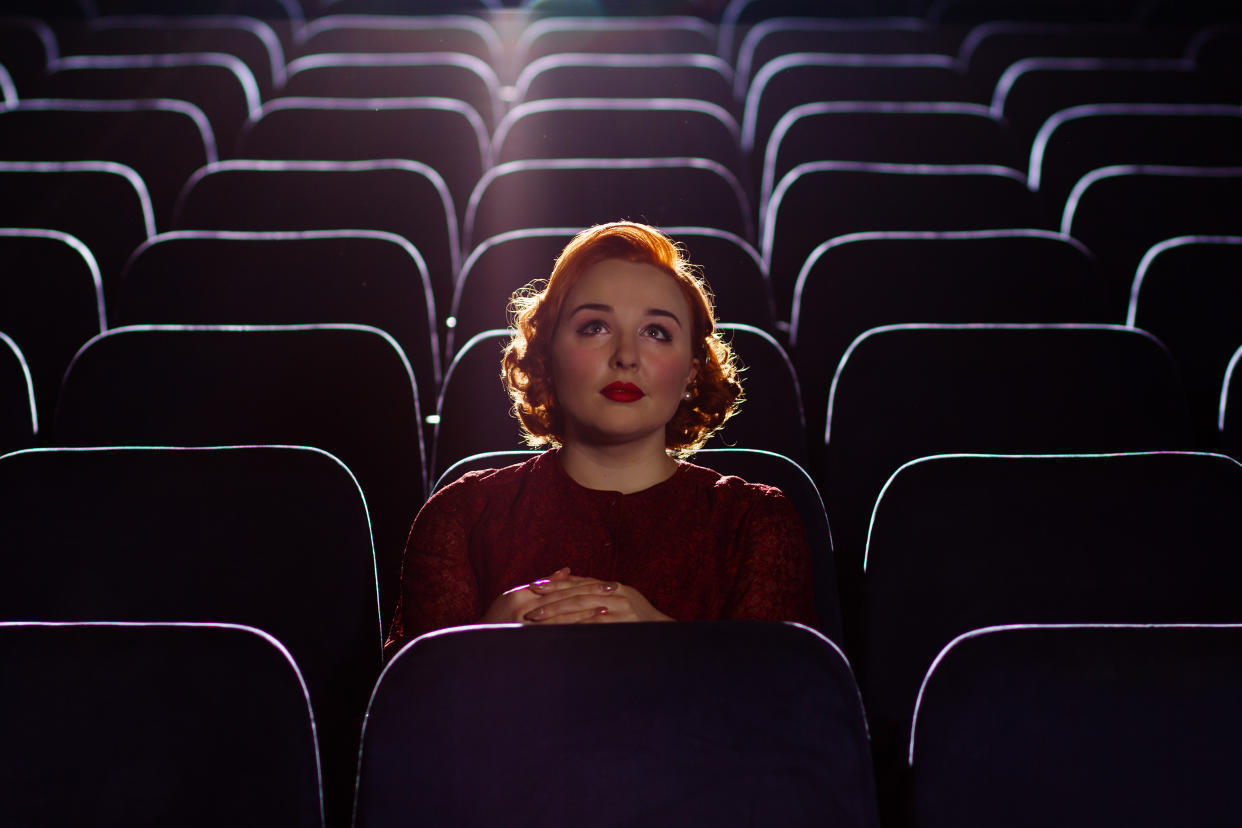 A beautiful young woman with red hair sits alone in a cinema.