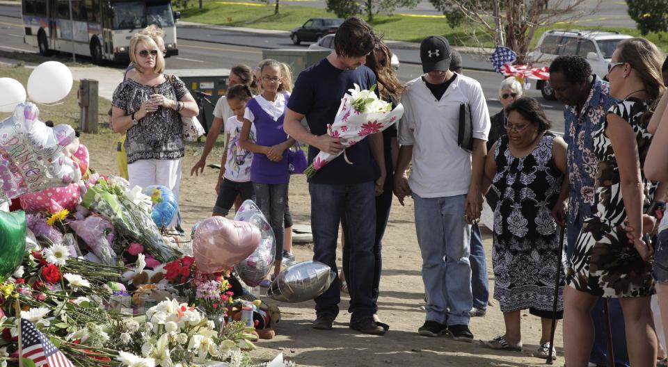 Actor Christian Bale, holding flowers at center, joins hands and prays with visitors to a memorial to the victims of Friday's mass shooting, Tuesday, July 24, 2012, in Aurora, Colo. Twelve people were killed when a gunman opened fire during a late-night showing of the movie "The Dark Knight Rises," which stars Bale as Batman. (AP Photo/Ted S. Warren)