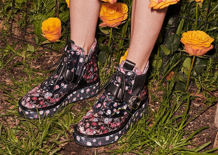 Someone standing in a garden wearing a pair of Coach leather boots, shown in black with pink floral print.