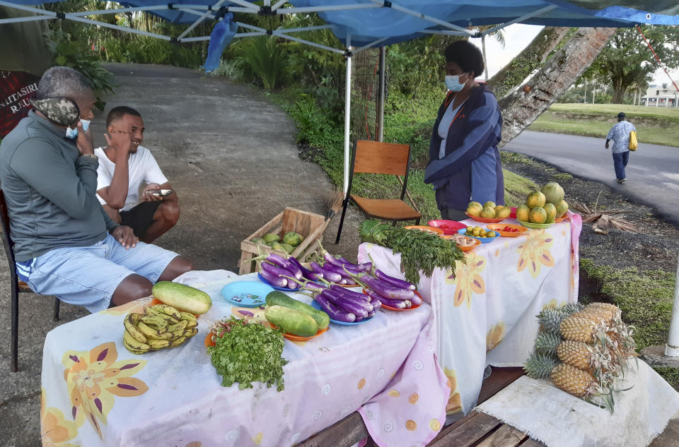 A family sells produce in front of their home in Suva, Fiji, Thursday, June 24, 2021. Mosese Soro, left, had to give up his business buying and selling fish because it can't operate while Fiji's borders are closed due to COVID restrictions. (AP Photo/Aileen Torres-Bennett)