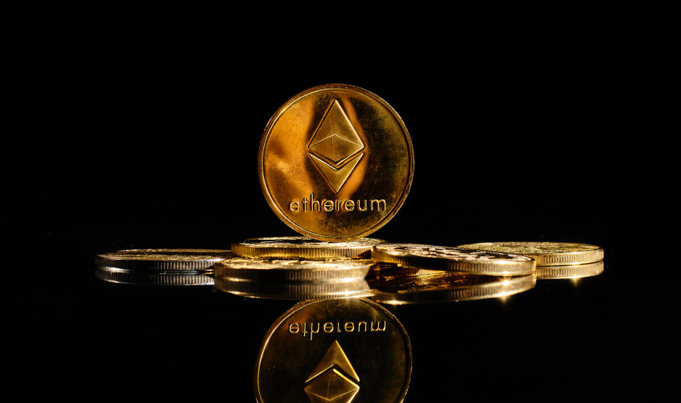 An Ethereum coin sits on top of Bitcoins on a black background.