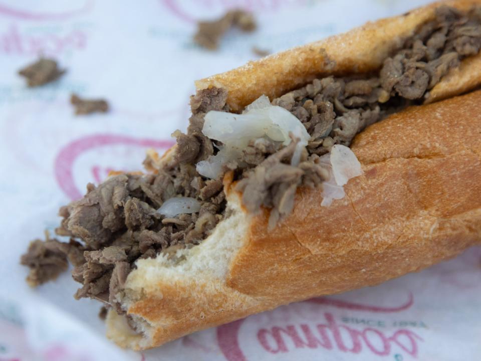 A half eaten cheesesteak with onions in a wrapper