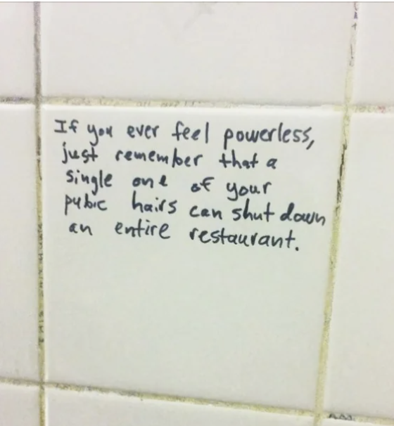 Handwritten text on a tile wall reads, "If you ever feel powerless, just remember that a single one of your pubic hairs can shut down an entire restaurant."