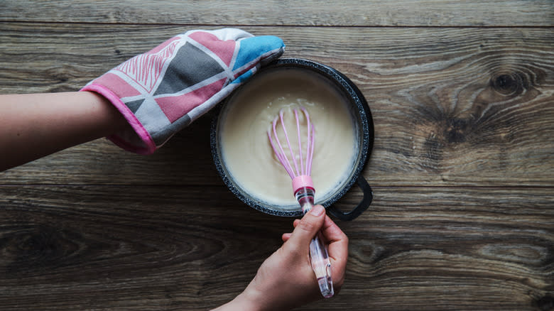 person whisking béchamel sauce