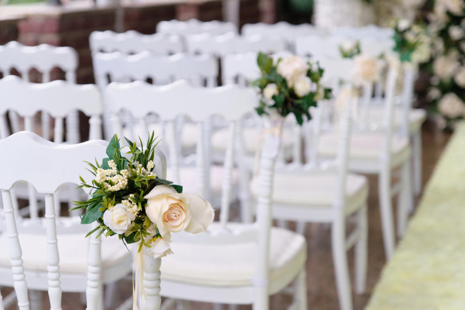 Rows of white chairs arranged for an event with floral decorations attached to the aisle seats