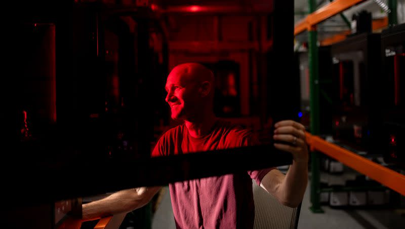 Spencer Loveless, CEO of Merit3D, an additive manufacturing company in Price, poses for a photo seen through the red-tinted door of one of the company’s LCD resin printers, which are a type of 3D printers, on Thursday, Aug. 17, 2023.