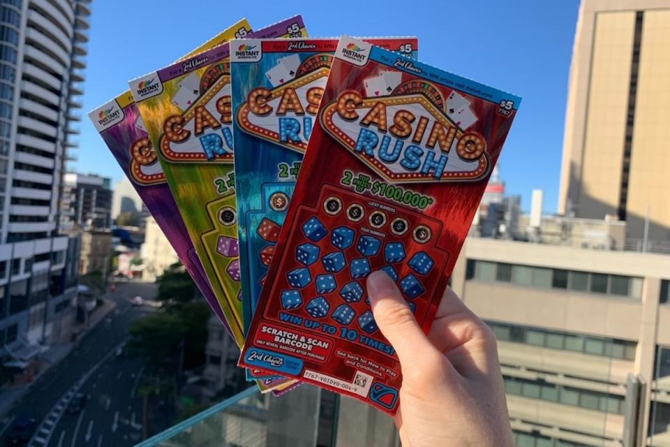 Hand holds winning scratchie tickets up on balcony of apartment building. Source: The Lott