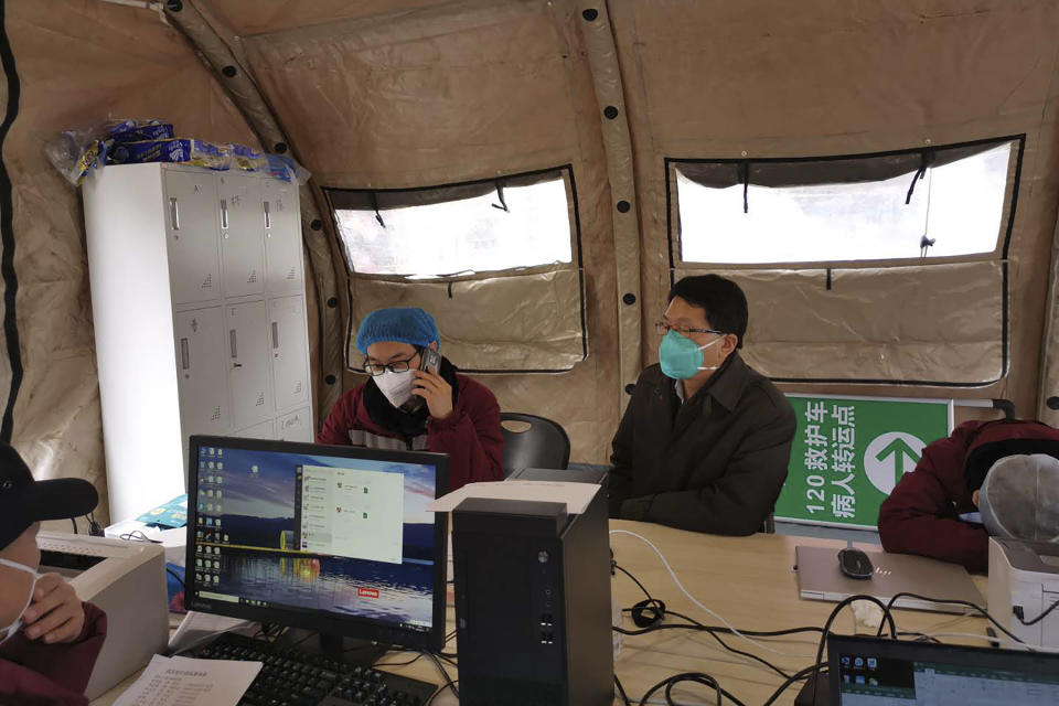 In this Feb. 14, 2020, photo released by Zhang Junjian, Zhang Junjian, center with green mask, head of the Wuhan Living Room Temporary Hospital works with his colleagues in a tent on the square in front of the temporary hospital in Wuhan in central China's Hubei province. The hospital is the largest of 16 temporary hospitals set up in gyms and other locations to handle an overflow of patients and try to stem the spread of the coronavirus by separating them from the rest of the city's 11-million inhabitants. (Zhang Junjian via AP)