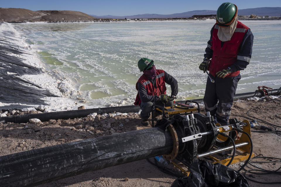 Workers perform maintenance at the pools where brine is evaporated at the lithium extraction plant facilities of the SQM Lithium company near Peine, Chile, Thursday, April 18, 2023. The metal is currently key in the global fight against climate change, used in electric car batteries, and crucial to solar and wind energy and more. But to extract it, mines suck water out of the flats, tethered to the lives of thousands of communities. (AP Photo/Rodrigo Abd)