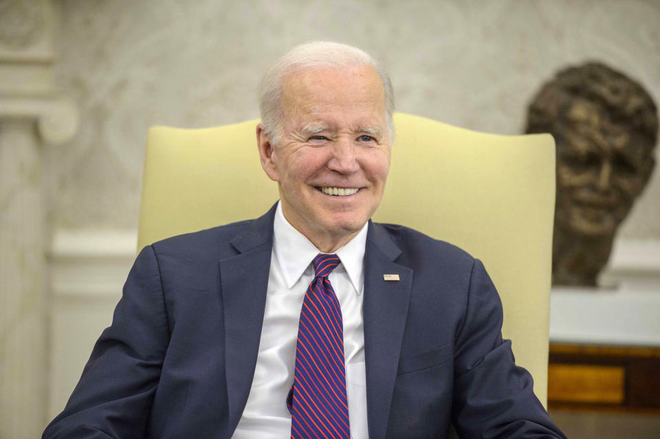 President Biden, smiling, sits in a yellow chair.