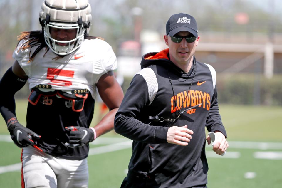 Oklahoma State defensive coordinator Bryan Nardo runs alongside sophomore safety Kendal Daniels between drills at the Cowboys' spring practice on Monday at the Sherman Smith Training Center.