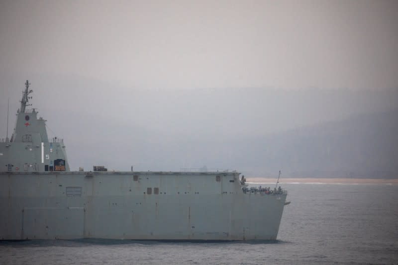 A member of the Navy is seen at the deck of the Royal Australian Navy vessel HMAS Adelaide as smoke blankets the area in the town of Eden