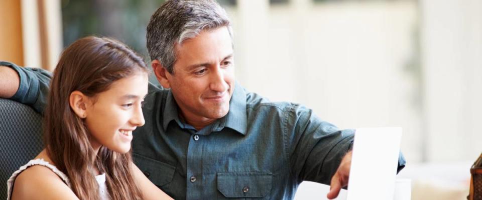 Father And Teenage Daughter Looking At Laptop Together